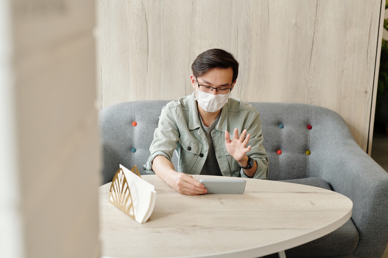 a men wearing mask waving hand in front of of his smart phone