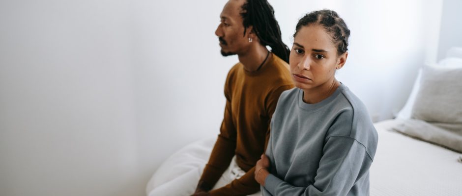 a man and a woman sitting on bed looking sad