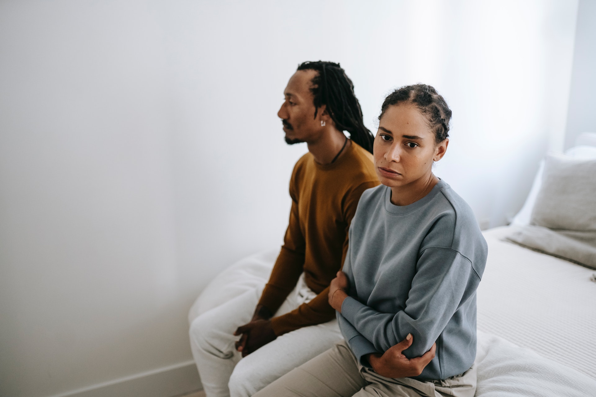 a man and a woman sitting on bed looking sad