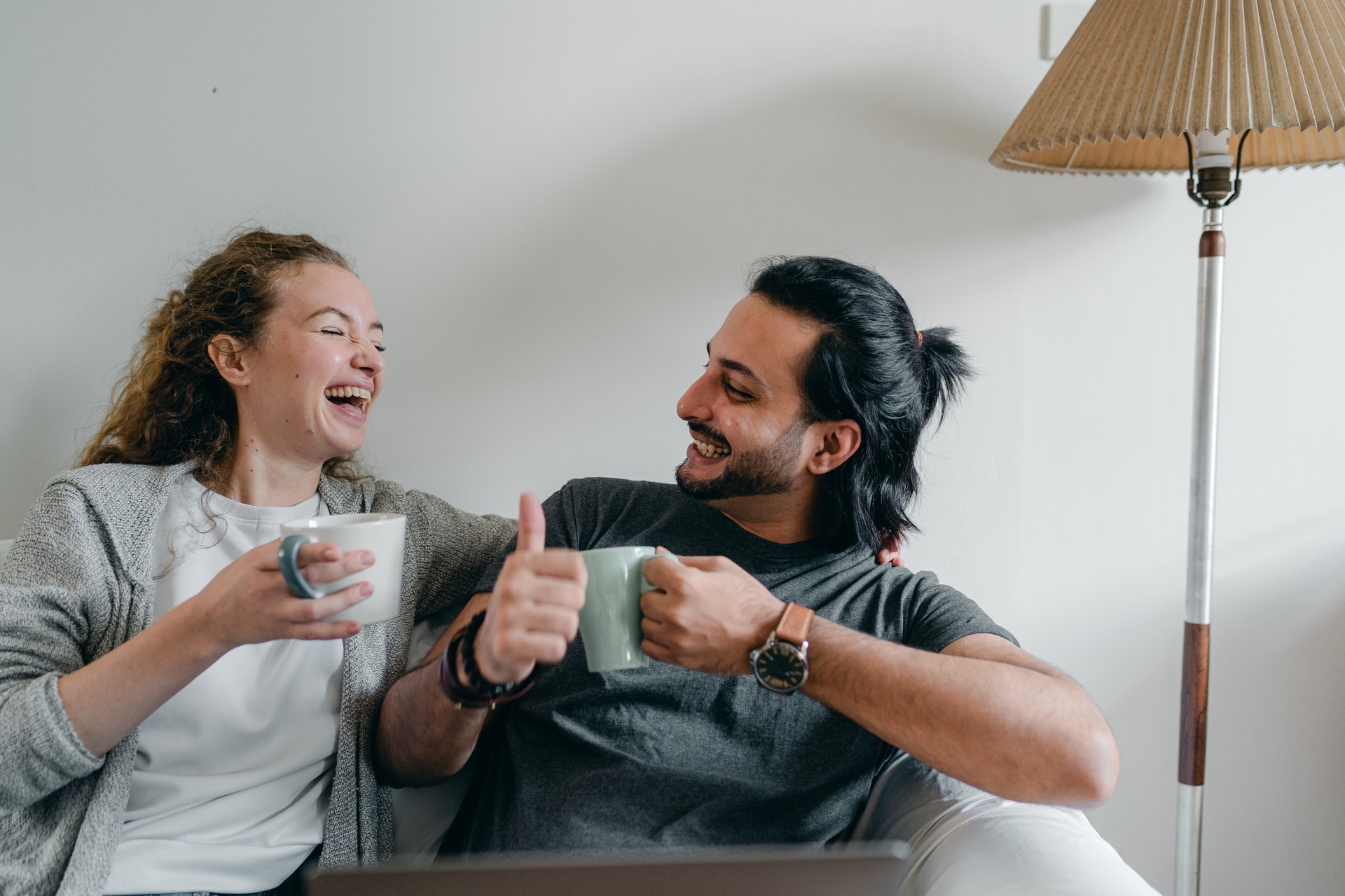 happy couple laughing on a couch and drinking coffee, having a deep conversation