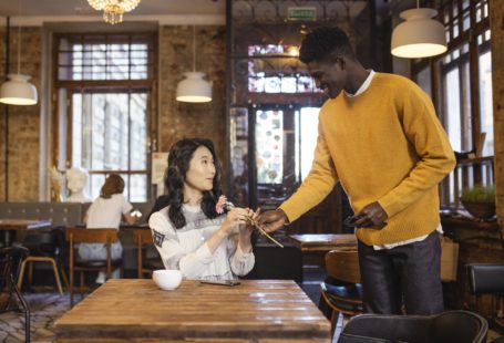 a black man giving flower to an asian woman on their first date at a coffee