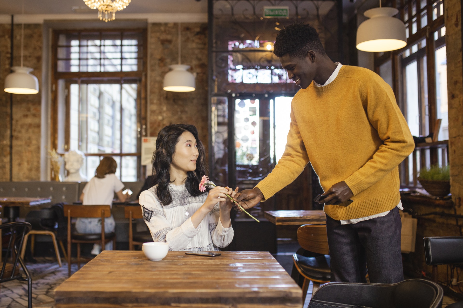 a black man giving flower to an asian woman on their first date at a coffee