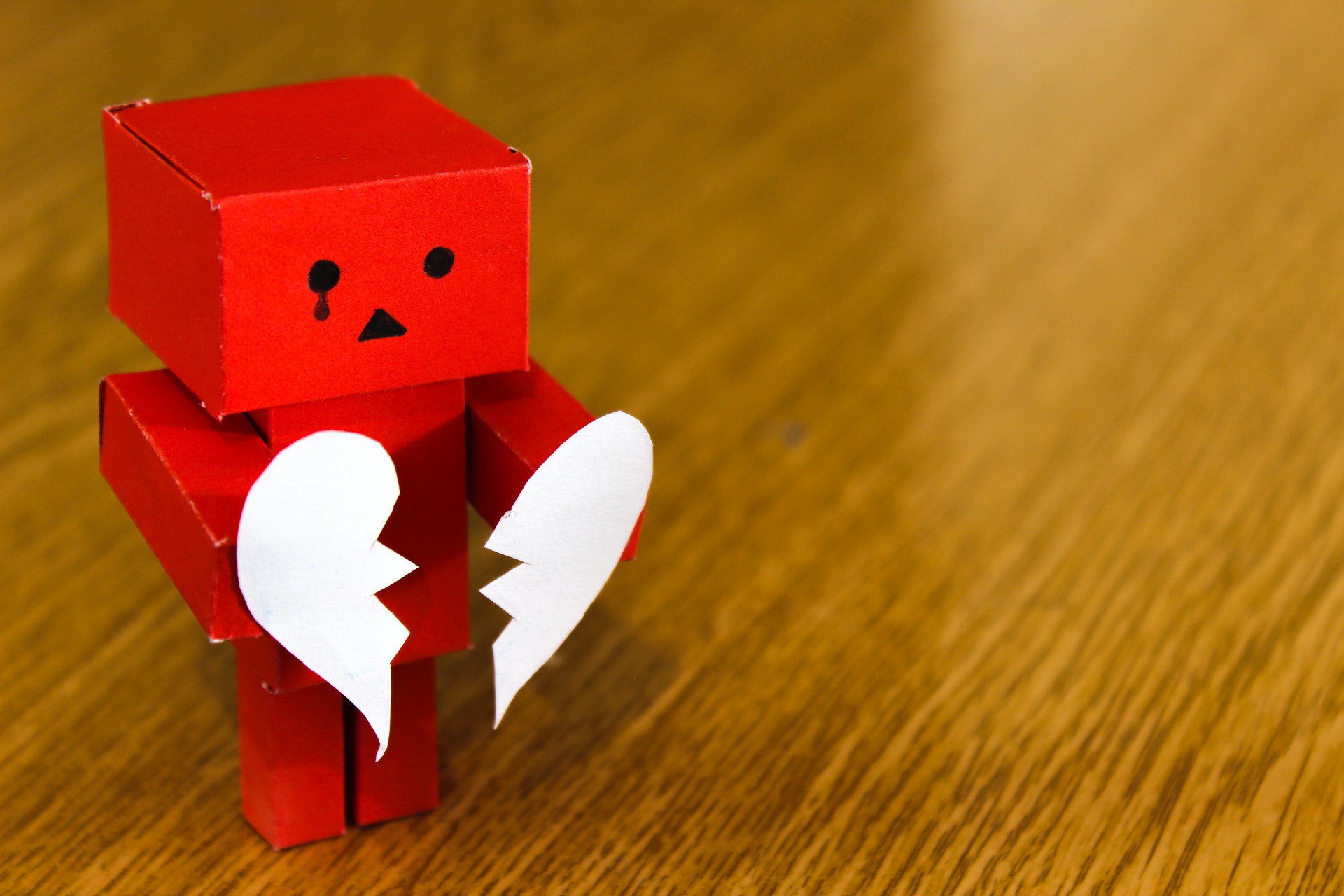 a wooden robot holding 2 pieces of a broken heart