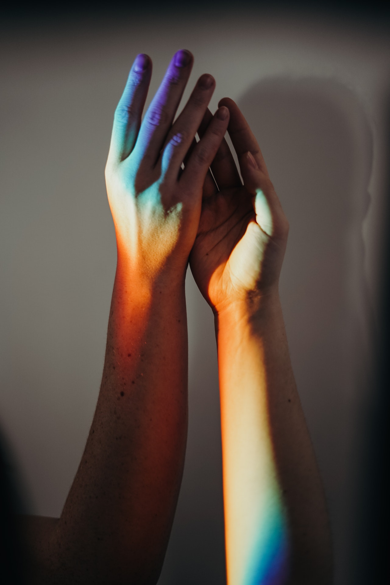 a close up photo of 2 hands holding in a shadow of LGBT rainbow color