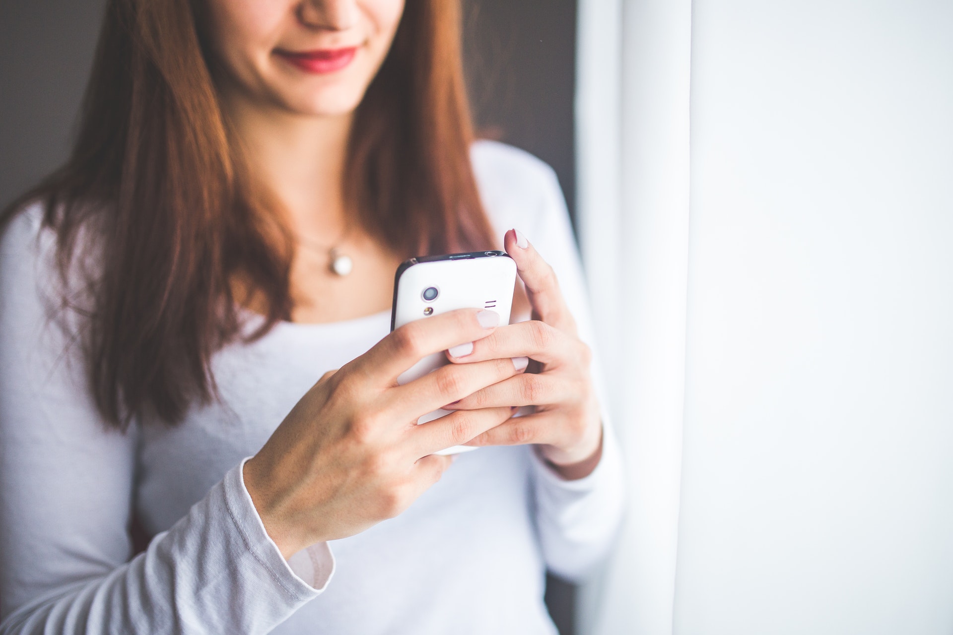 a woman in white shirt is using mobile phone for texting