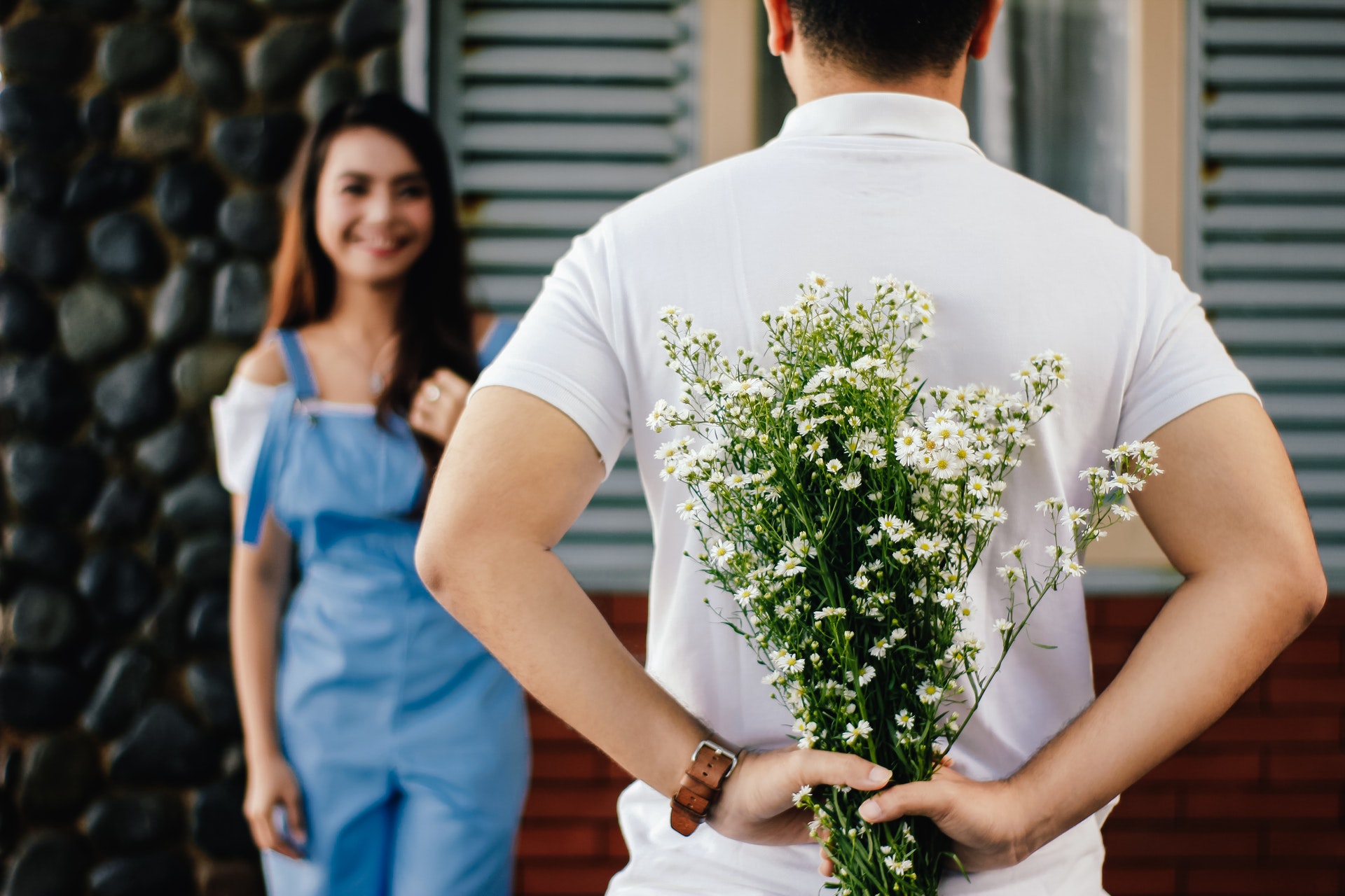 a man hiding flowers behind his back to surprise a woman