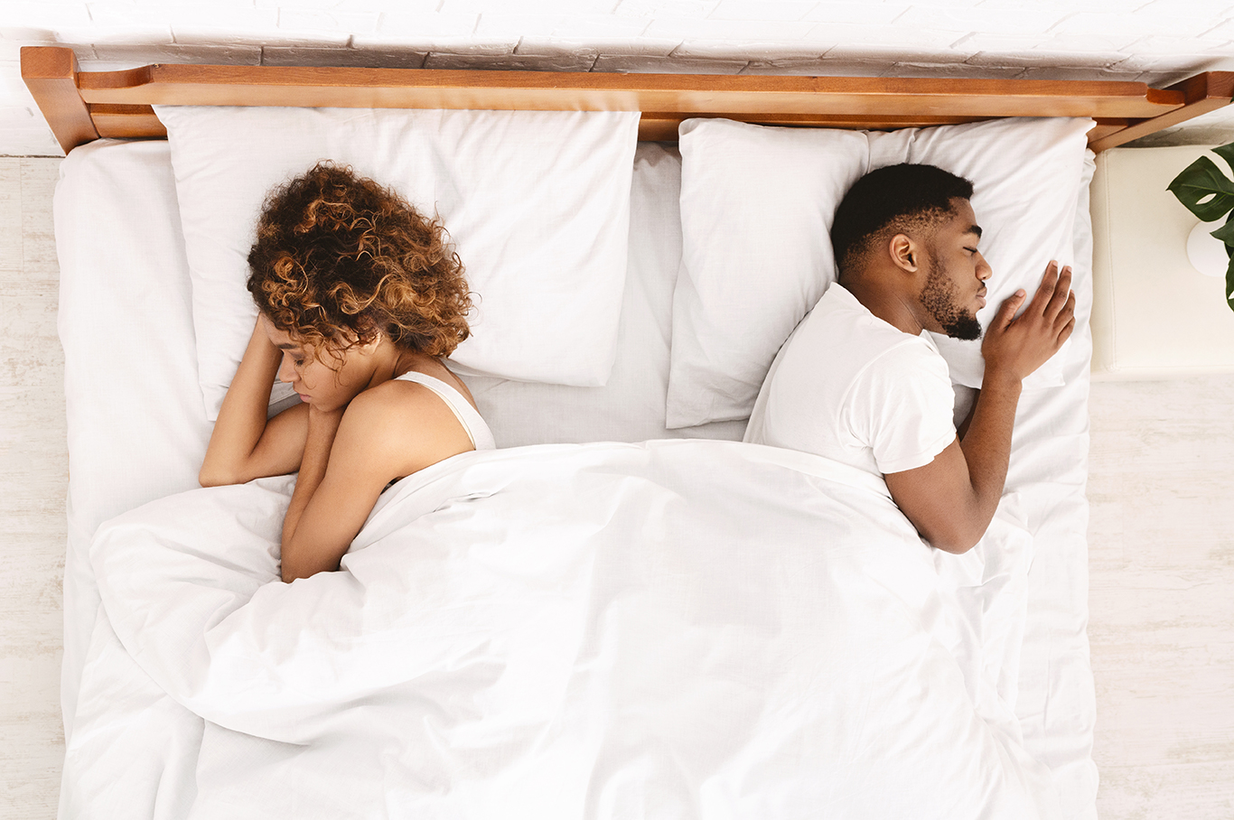 An image of a black man and a white woman sleeping on a bed, facing away from each other, symbolizing emotional distance and relationship challenges.
