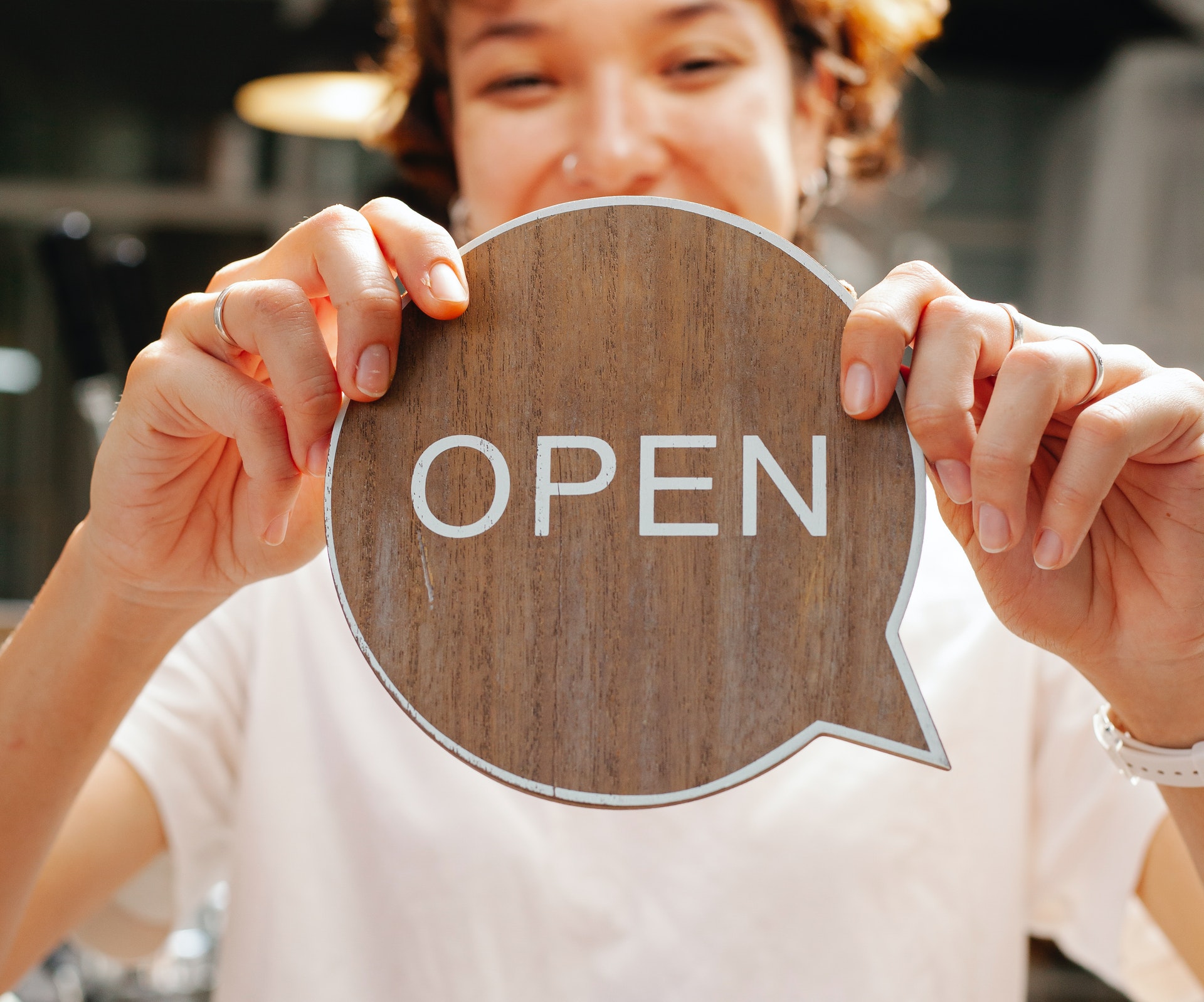 a woman holding an wooden signboard saying open