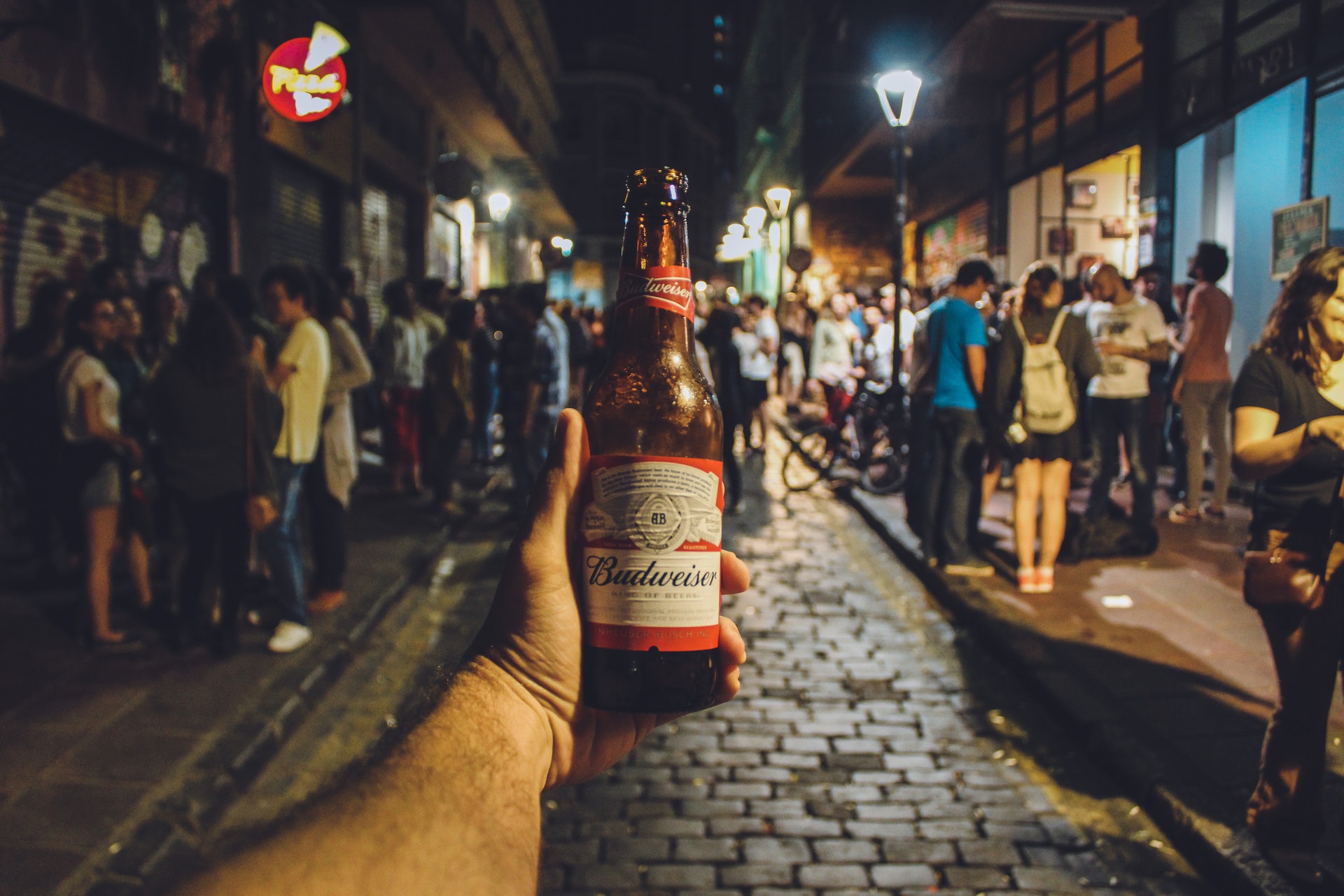 a hand holding a bottle of Budweiser in a bar crawl night